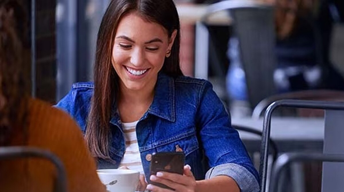 A woman at a coffee shop looks down at her smart phone.