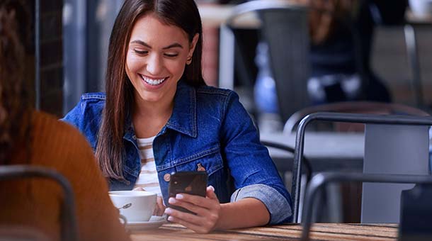 A woman at a coffee shop looks down at her smart phone.