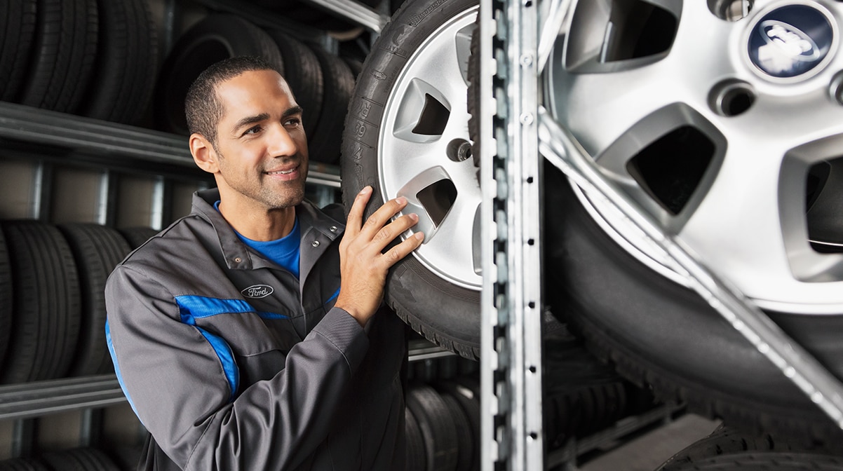 A Ford Service Technician pulls a vehicle tire from a shelf.
