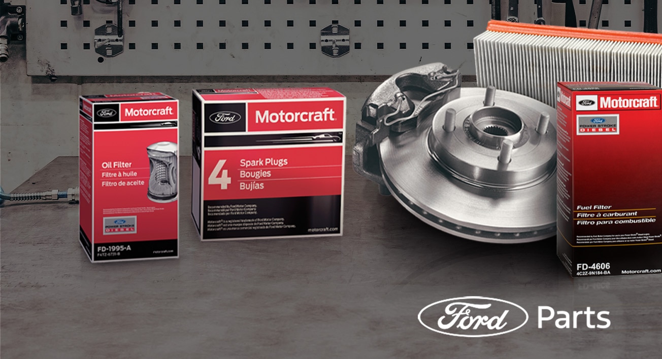 Motorcraft auto parts on a workbench, including an oil filter, spark plugs, brake rotor, and air filter. 