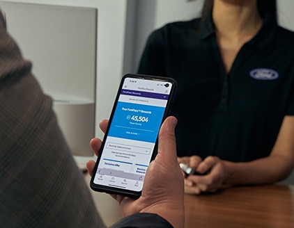 Person holding a smartphone with the FordPass app open, and FordPass Rewards points displayed.   