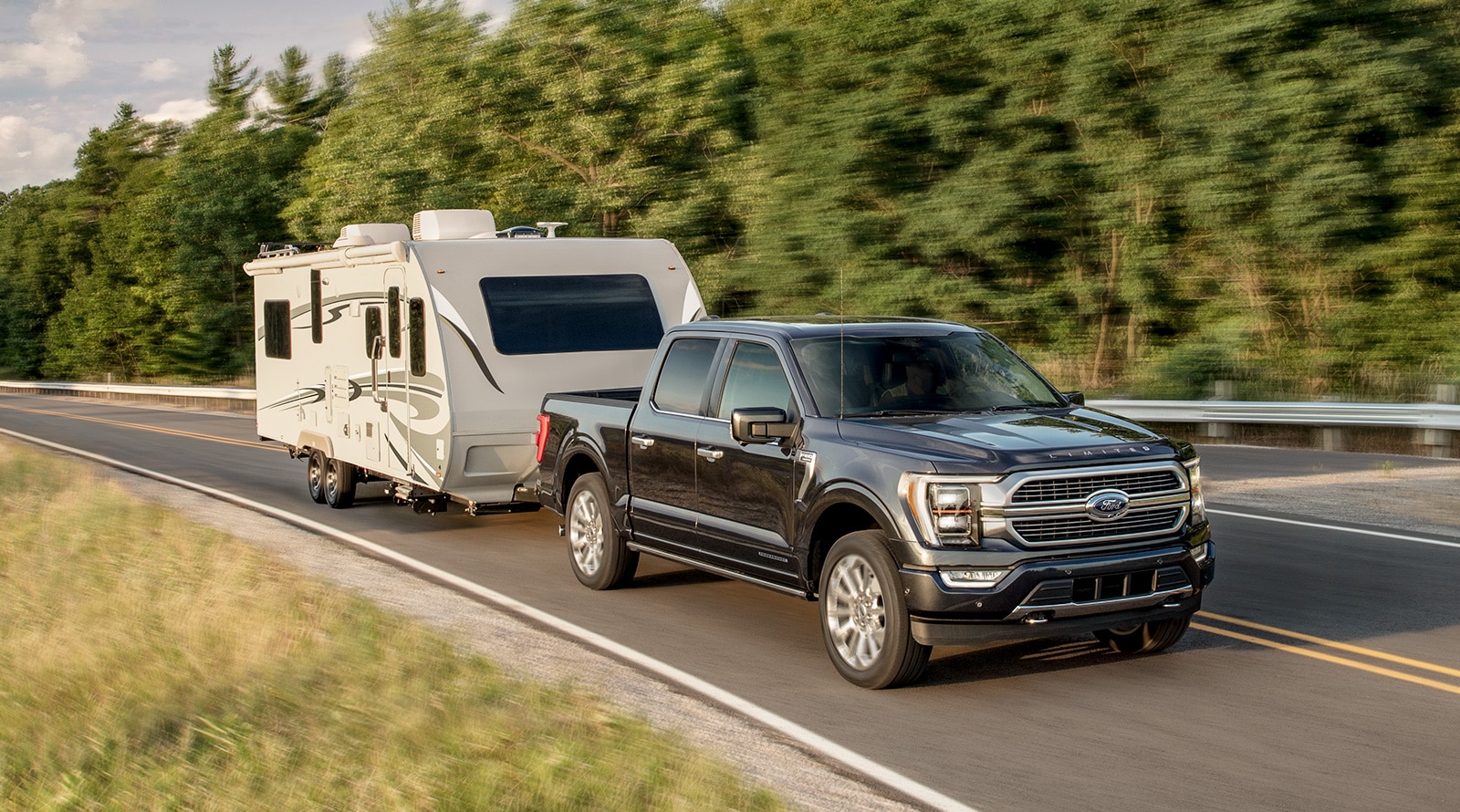 A Ford F-Series pickup truck towing a camper trailer on a highway.