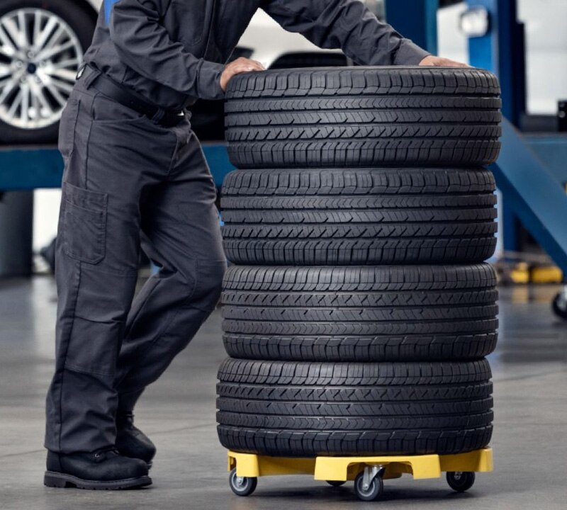 A Ford Service Technician pushing a stack of four tires on a drum dolly.