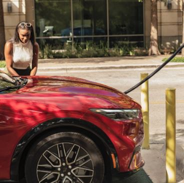 A woman stands next to a red vehicle connected to a charging station