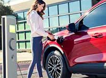 A person is standing next to an electric vehicle at a public charging station