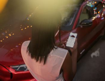 A person is standing next to a red electric vehicle looking at a smartphone