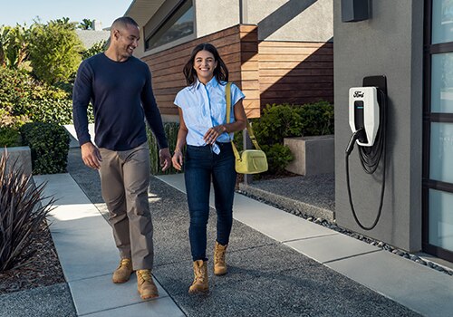 A man and a woman walk in front of a Ford Connected Charge Station.