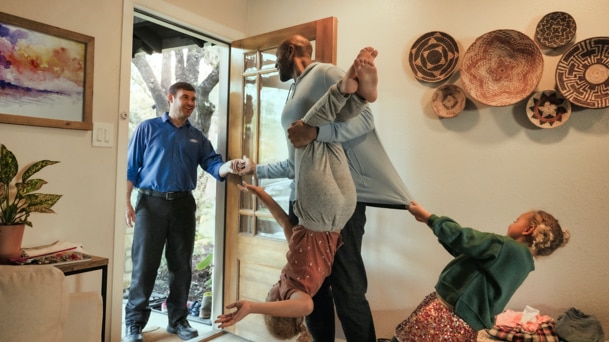 A man hands off his keys to a Ford adviser while two children are grabbing onto him to get his attention.