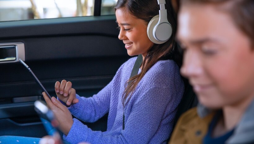 Niño y niña en el asiento trasero de un auto usando el Hotspot Wifi de FordPass Connect