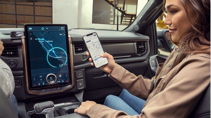 Una mujer sostiene un smartphone con la Aplicación FordPass en la pantalla en frente de una Mustang Mach-E que se está cargando.