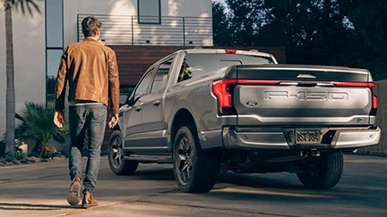 A man walking near his Ford F-150 truck outside of a home.