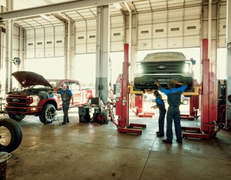 Three service technicians working on two Ford trucks in a service bay.