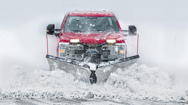 Red Ford pickup plowing through snow.