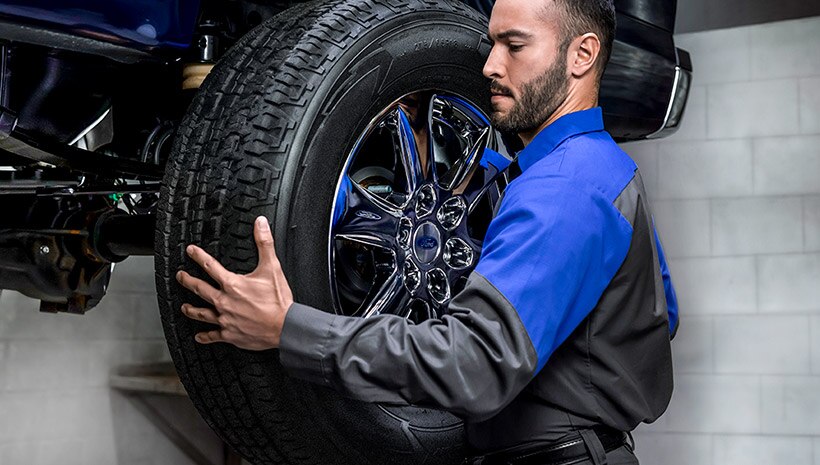 Ford® Service technician pulling vehicle off of tire rack to show customer