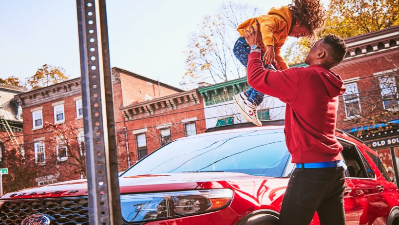 Un hombre parado al frente de la Ford Explorer en Rapid Red sosteniendo a un niño sonriente en el aire
