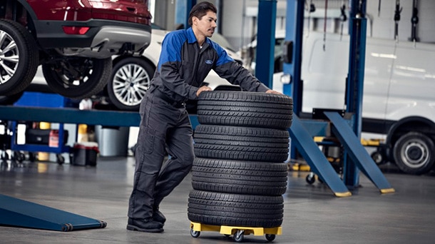 Ford service technician moving wheeling a stack of 4 tires across service bay floor