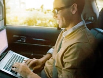A man typing on a laptop in the back passenger-side seat.