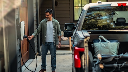 A person has parked a Ford EV in their driveway and reaches for a charger.