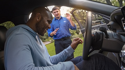 A driver seated in a Ford vehicle with the door open gets assistance from a Ford technician.