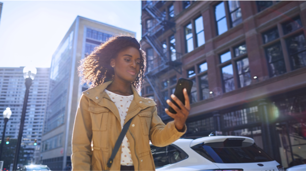 GUARDA LA FECHA Una joven negra con una chaqueta amarilla mirando el calendario de su teléfono mientras camina al lado de edificios altos de ladrillo