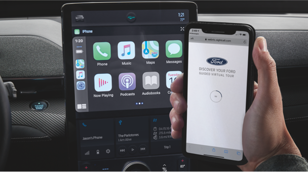 ABRÓCHATE EL CINTURÓN DE SEGURIDAD Propietario de un Ford sosteniendo su teléfono y cargando el Recorrido Virtual Guiado en su teléfono junto a la pantalla de SYNC en su automóvil