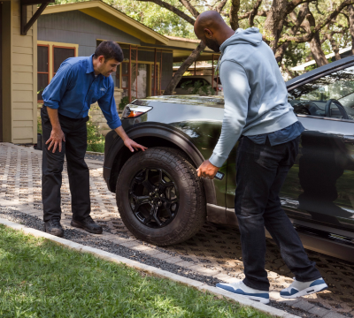 Two men examine the tires of a Ford Explorer SUV parked in a driveway