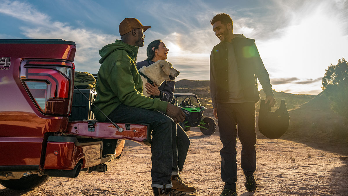 A group of friends and their dog gather around an open F-150 tailgate after riding 4-wheelers on a mountain.