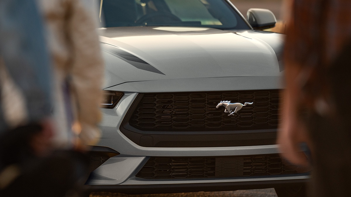 The grille of the 2025 Mustang® coupe comes into focus behind two people walking.