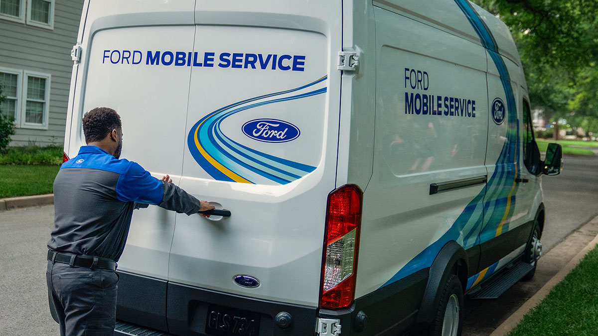 A Ford Mobile Service technician opens the back door to the service van outside a home.