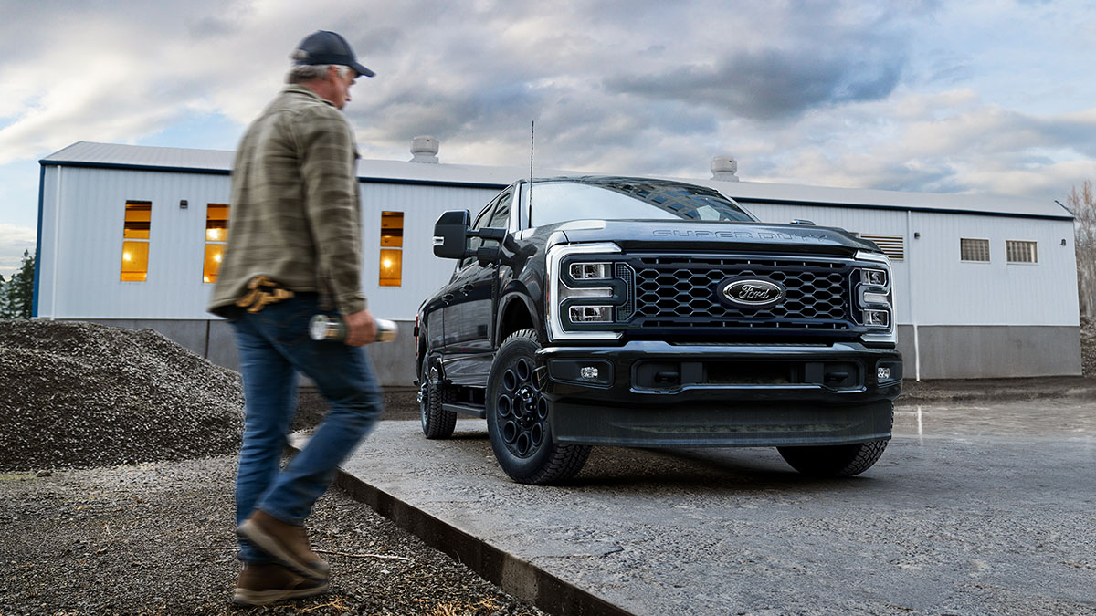 A worker approaches a Super Duty® truck parked heroically in front of a building at a worksite.