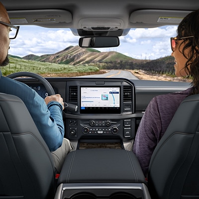 A couple drives a Super Duty ® truck on a two-lane highway through a hilly area, with the center screen lit up between them.