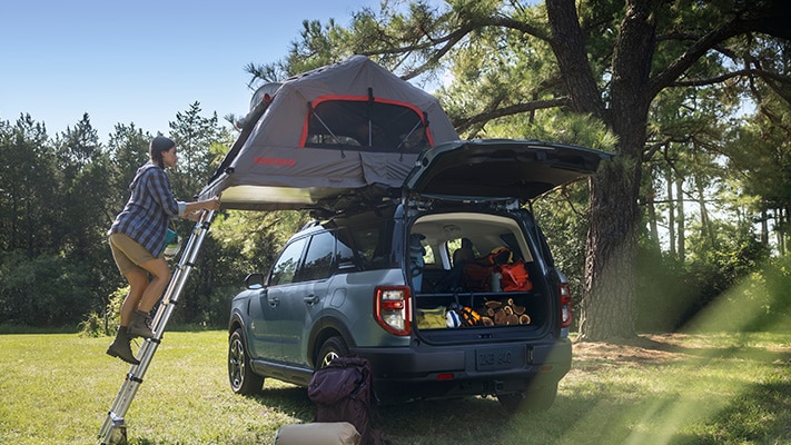 An owner climbs a ladder into their roof-top tent on top of their Bronco Sport® SUV