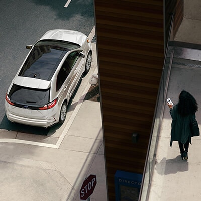 A driver looking at a smartphone and walking near a parked white 2023 Ford Edge® SUV.