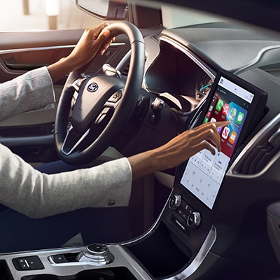 A driver touching the SYNC® 4A Technology touchscreen in a Ford Edge® SUV, which is displaying the Apple CarPlay® interface.