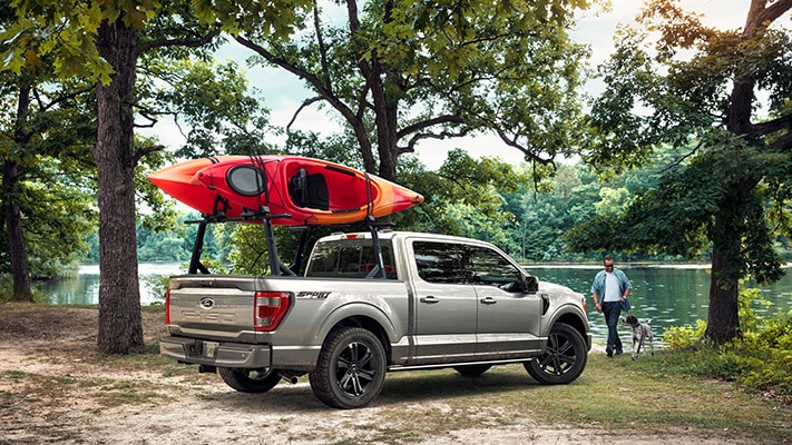 The F-150® pickup loaded up with a couple kayaks sits parked beside a lake.  