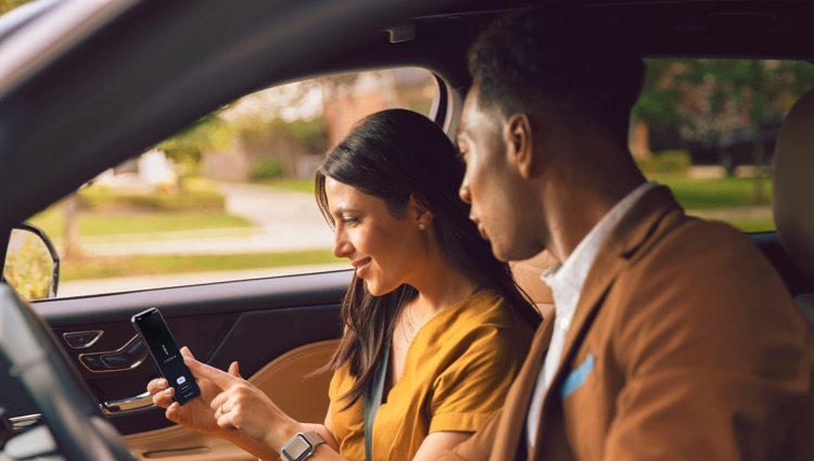 Un hombre y una mujer se sientan dentro de un vehículo Lincoln viendo la aplicación Lincoln Way en un smartphone.