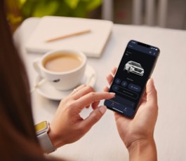 Una persona sostiene un teléfono inteligente y ve la aplicación Lincoln Way frente a una taza de café.