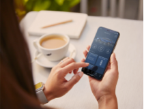 Una mujer sosteniendo un smartphone y viendo la aplicación Lincoln Way frente a una taza de café.