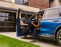 A person is shown sitting in the drivers seat of a Lincoln® vehicle while using their smartphone