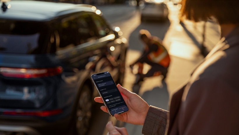 A person is holding a smartphone while receiving roadside assistance on their vehicle.