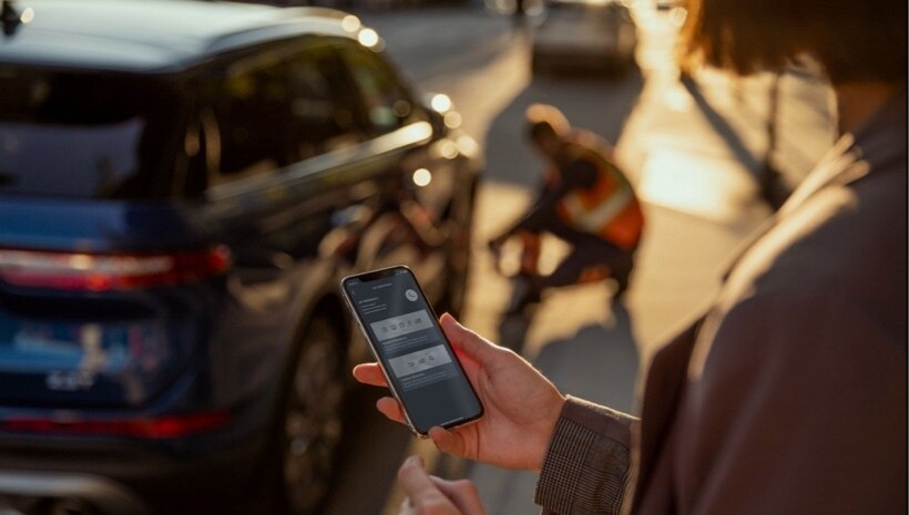 A person is seen holding a smartphone in their hand while receiving roadside assistance on their vehicle