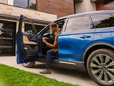 A person is shown seated in the drivers seat of a parked Lincoln using their smartphone