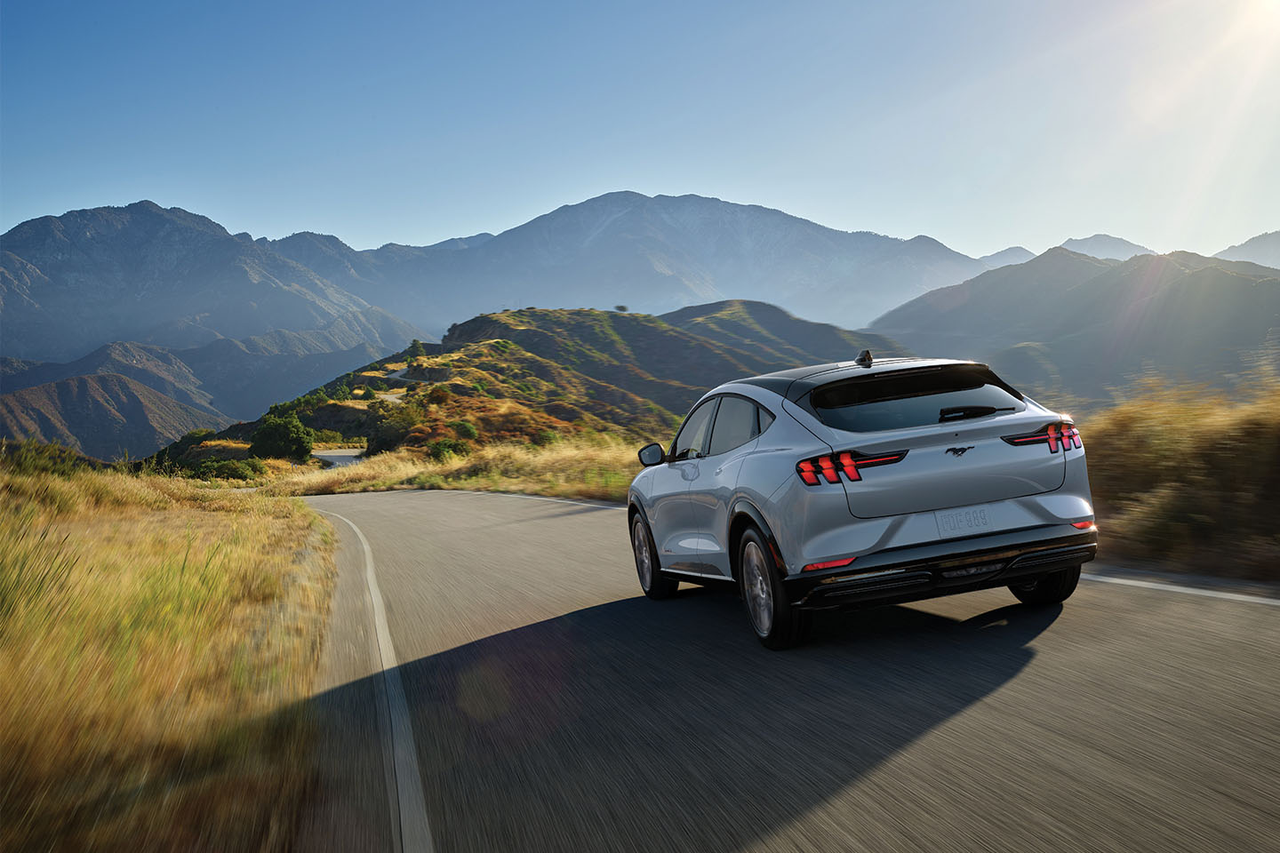 A Ford Mustang Mach-E is driving on the highway through the mountains.