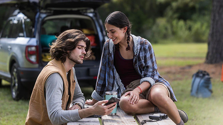 Two people seated at a picnic table near a 2023 Ford Bronco® Sport SUV with available Ford Accessories in the background.