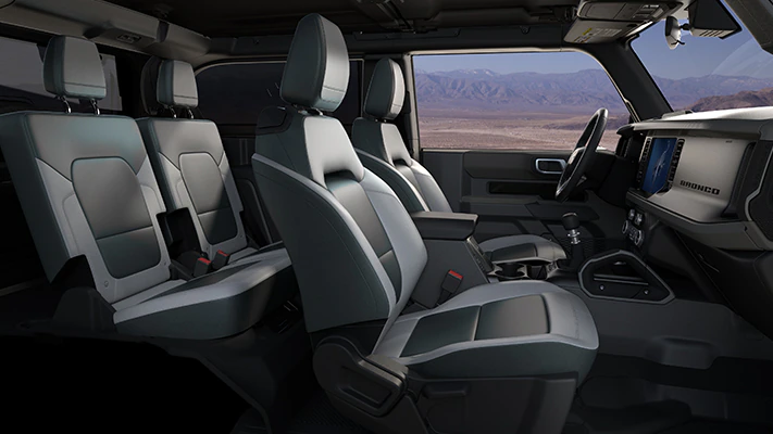 A 2024 Ford Bronco® Big Bend® SUV’s gray interior with optional equipment shown and rugged desert scenery outside its window.