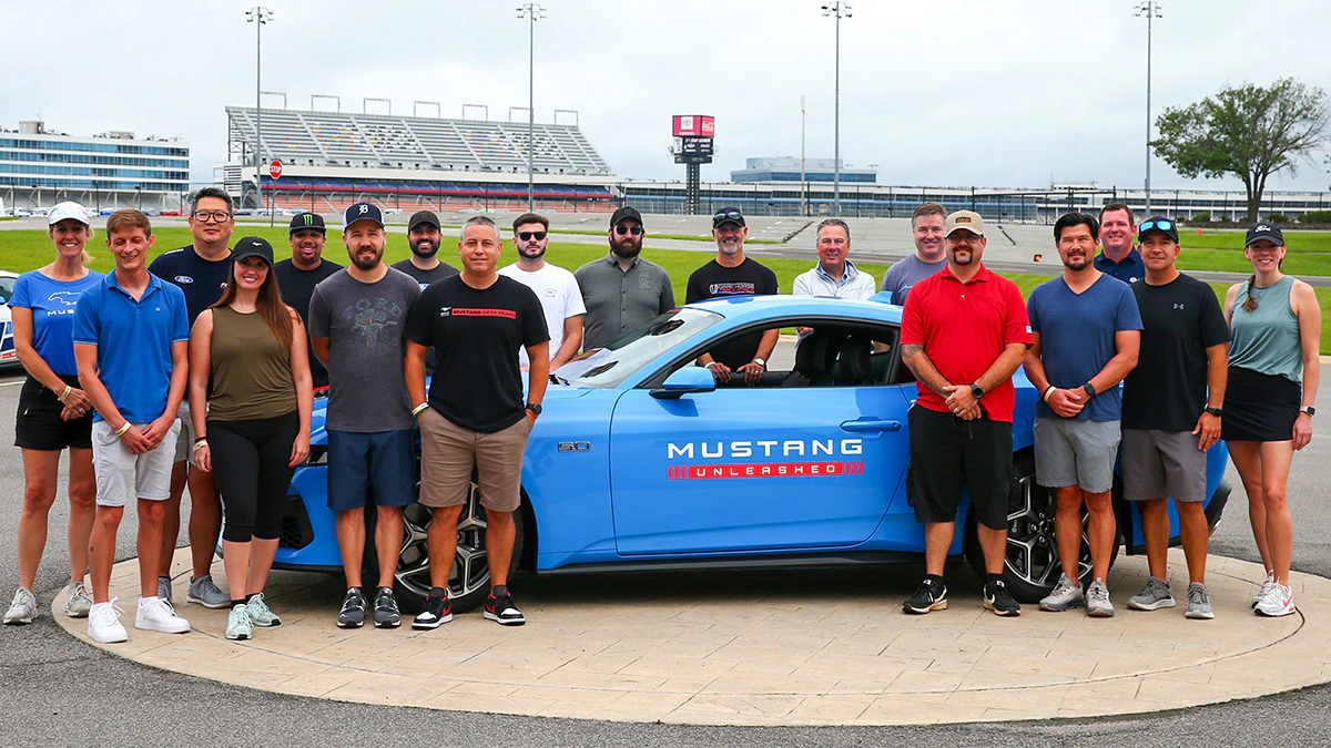 A group of enthusiasts stand in front of a Mustang® at a Mustang Unleashed event.