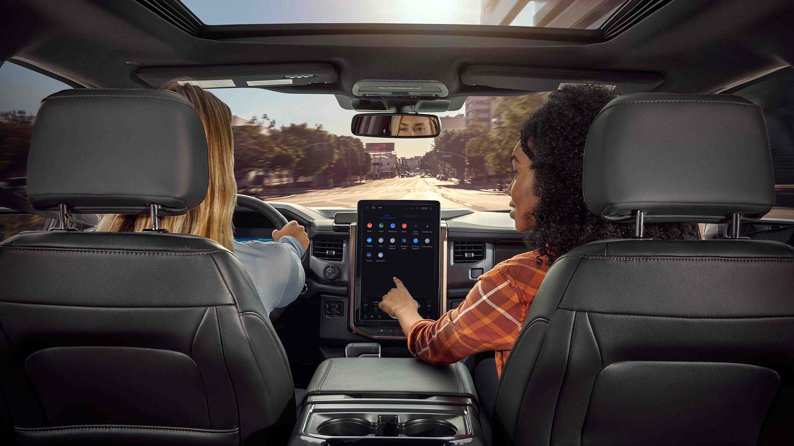 A driver in a Ford vehicle looking ahead while their passenger uses the available technology touchscreen navigation feature.