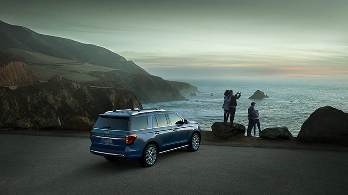 A blue 2023 Ford Expedition® Platinum® SUV parked by a seaside area at dusk with people enjoying the view nearby.