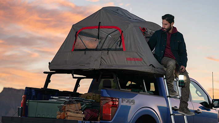 An F-150® truck owner climbs down from their roof-top tent.