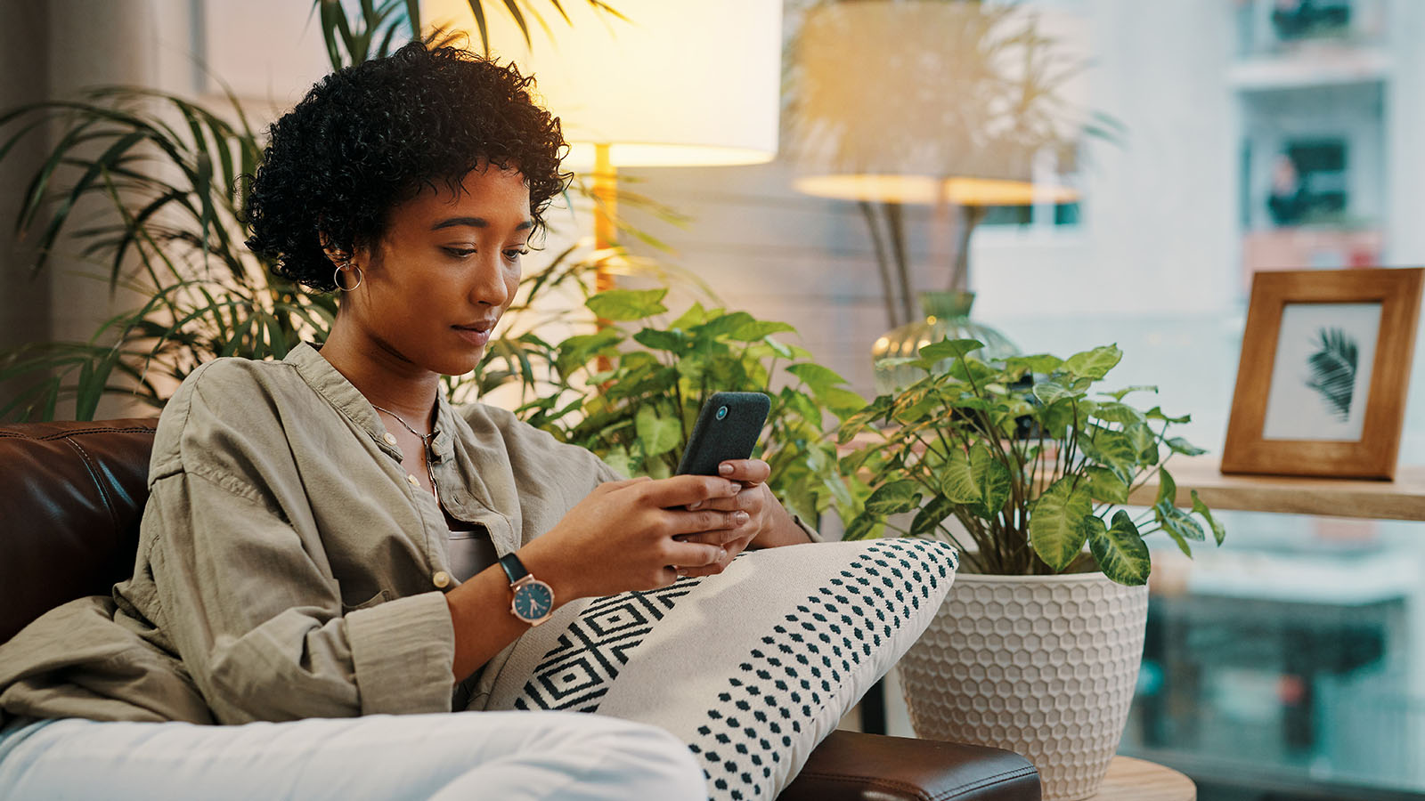 A young professional looking at the FordPass® app on a smartphone while relaxing at home.